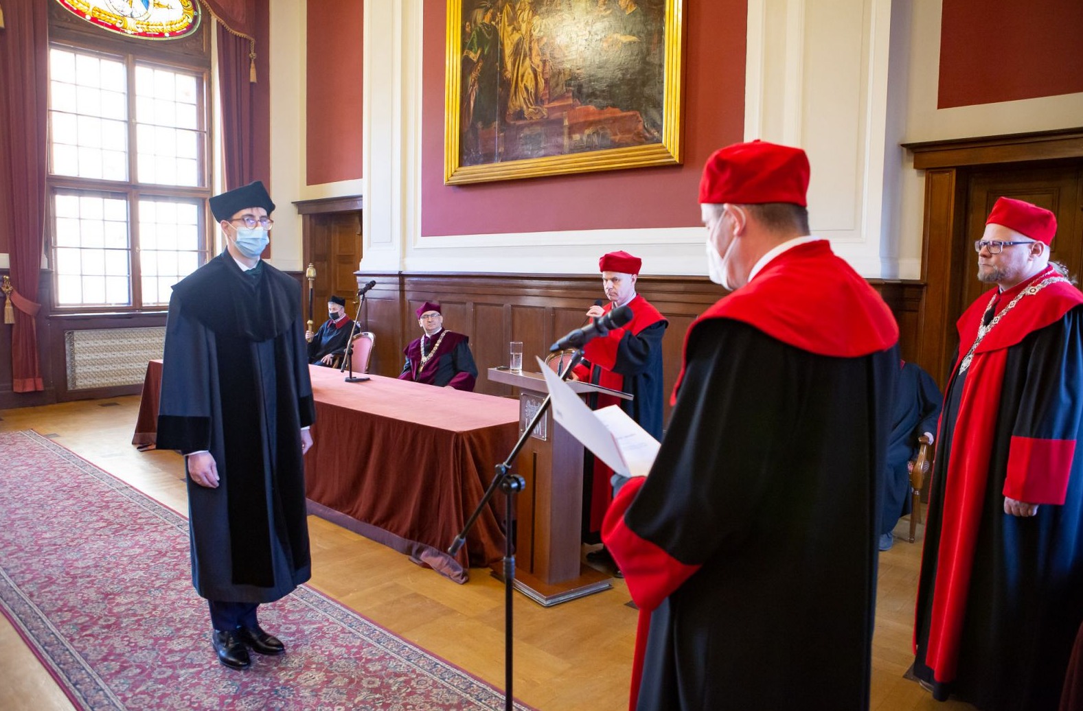 na zdjęciu promowany, dziekani, prorektor za stołem prezydialnym i promotor