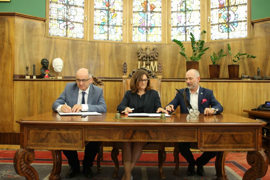 trzy osoby podpisujące umowę siedzą za biurkiem w gabinecie Rektora