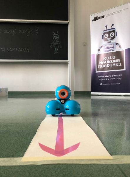 zaprezentowany mały robot na tle plakatu z logo koła Naukowego Robotyki 