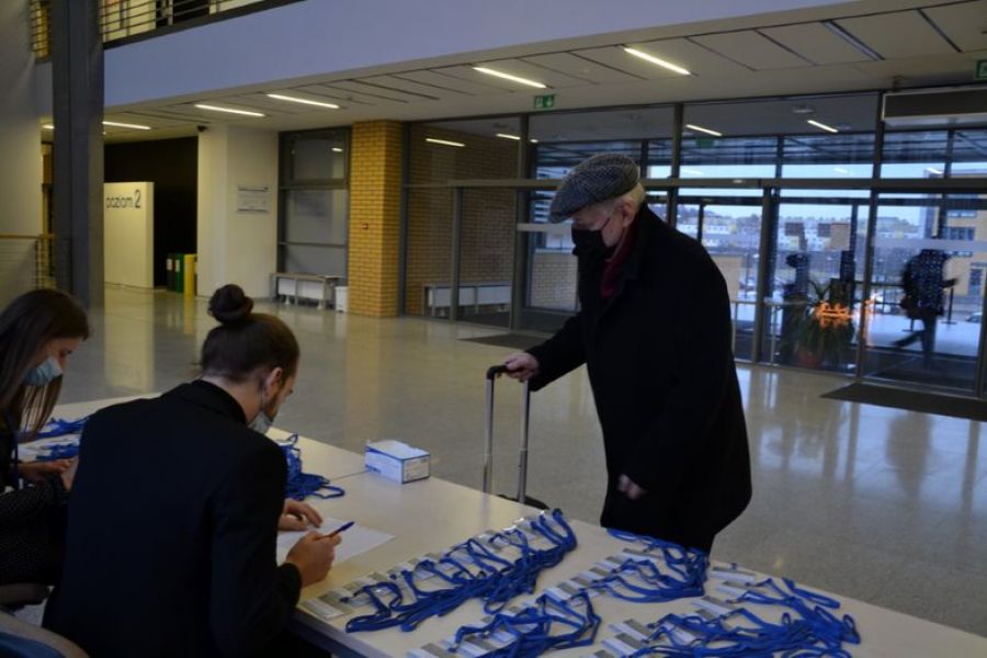 na zdjęciu w holu wydziału, przy stoliku młoda kobieta i mężczyzna rejestrują uczestnika sympozjum